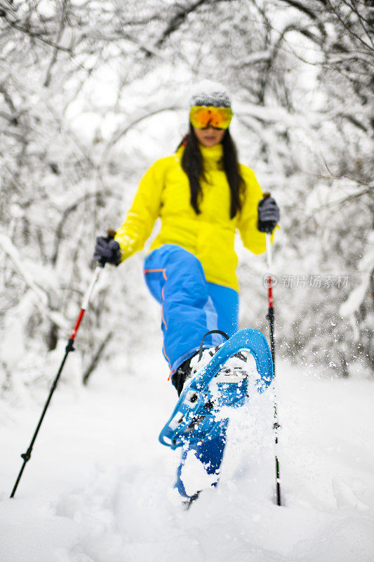 一名女冒险家穿着雪鞋在冰雪覆盖的森林里穿过厚厚的积雪