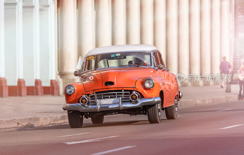 古巴出租车司机开着一辆橙色的老爷车穿过古巴哈瓦那老城区