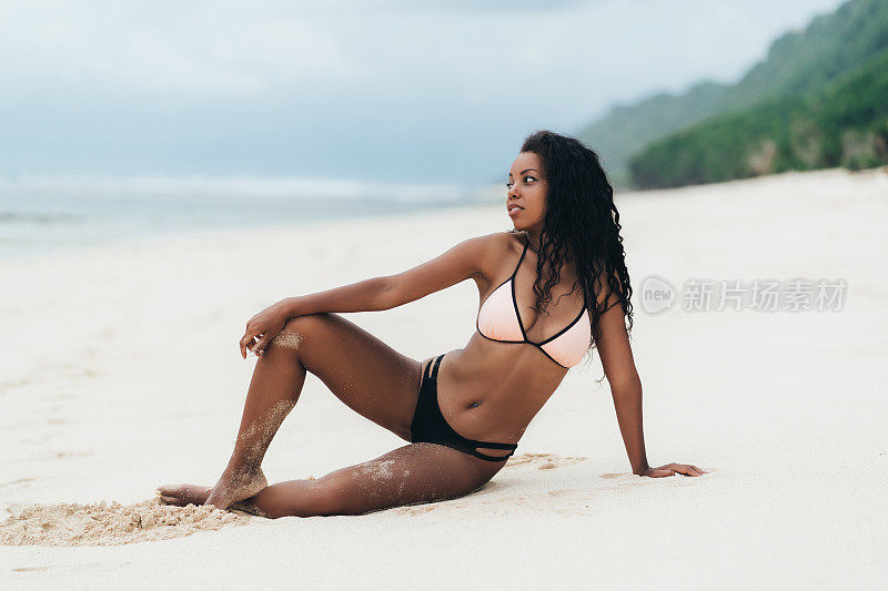 苗条性感的黑皮肤的女孩在泳装摆姿势在沙滩上的沙子。美国黑人妇女在天堂岛休息
