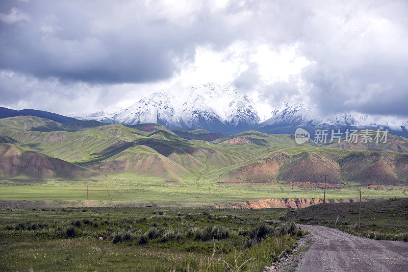 碎石路在开花的田野和风景如画的山脉之间的地平线上。吉尔吉斯斯坦Naryn地区