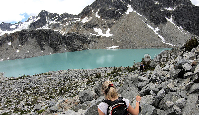 徒步旅行者穿越高山湖泊上方的巨石田