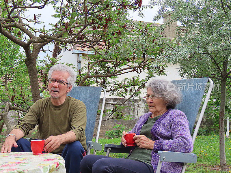 一对活跃的老夫妇在房子的后院喝清晨咖啡