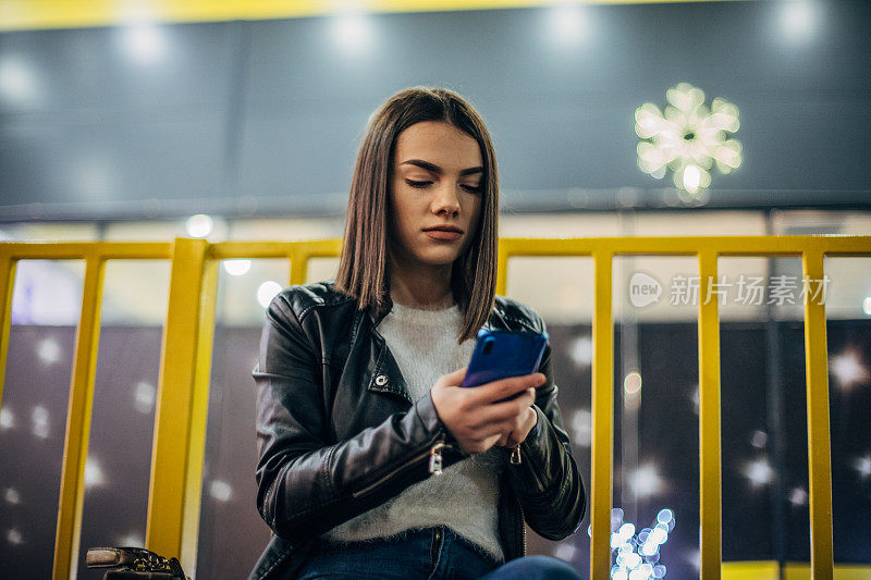 漂亮的年轻女子坐在长椅上玩手机