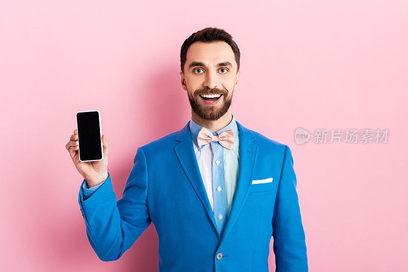 快乐的大胡子商人拿着粉色空白屏幕的智能手机