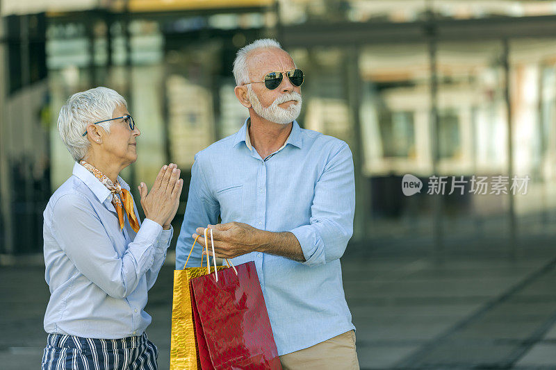 一对老年夫妇拿着购物袋走在城市街道上争吵