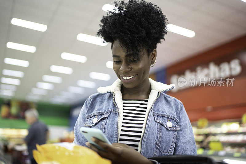微笑的年轻女子拿着产品在超市和搜索的电话