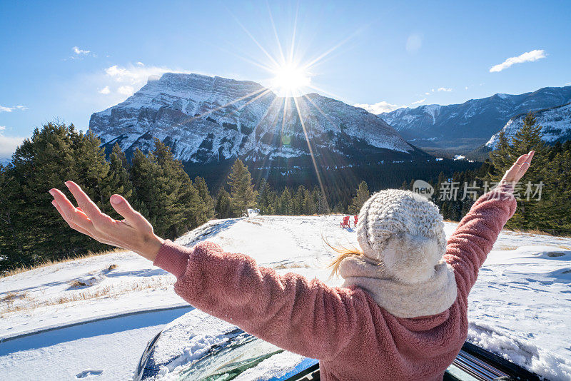 年轻女子在雪山公路上从车里伸出双臂