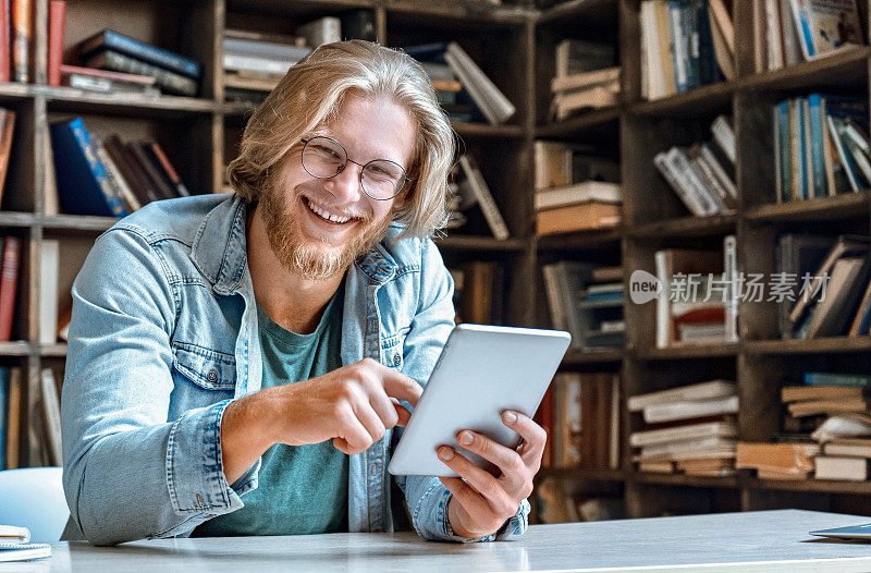 肖像年轻的大胡子男子学生商人时髦的教师眼镜办公室家庭图书馆书桌持有现代的平板电脑平板电脑使用应用触摸屏微笑大笑信息观看视频看相机复制空间