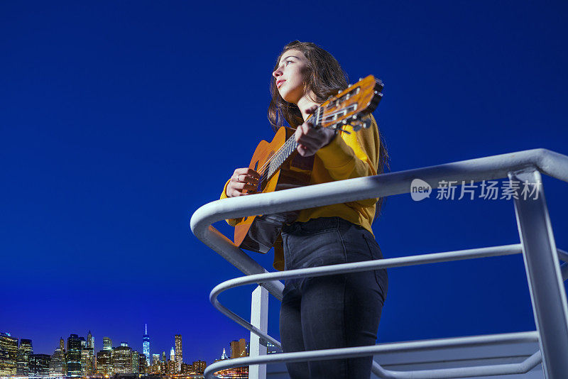 少女弹吉他从家阳台在蓝小时看纽约曼哈顿