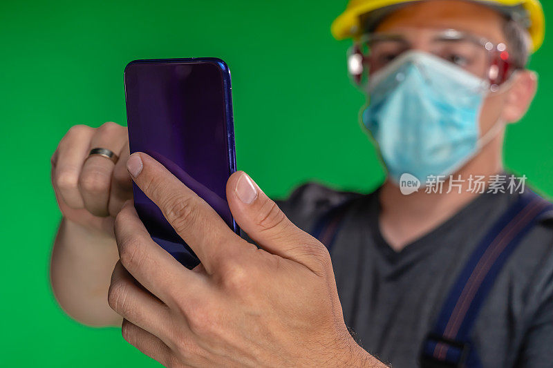 建筑工人戴着N95防护面罩和头盔使用智能手机