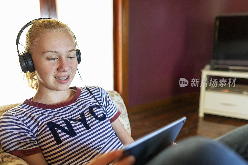 十几岁的女孩在家里戴着耳机和平板电脑