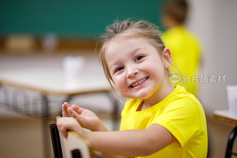 微笑的女学生看着镜头坐在教室的椅子上