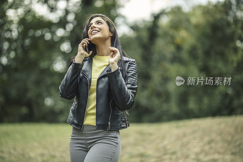 快乐的年轻女子微笑和使用她的手机在户外