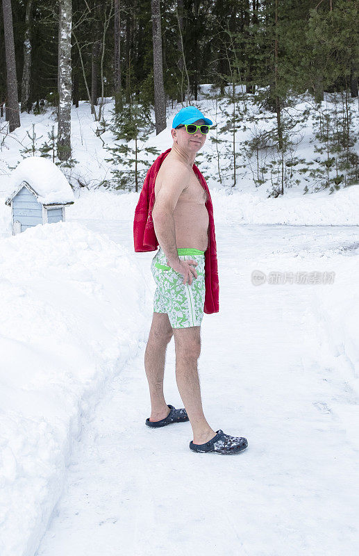 一名身穿泳裤和沙滩浴巾的白人男子沿着积雪覆盖的乡村道路去蒸桑拿。桑拿和芬兰传统。