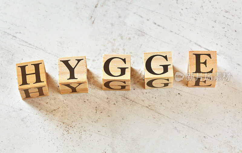 五个木制立方体，字母HYGGE(斯堪的纳维亚语，意为舒适的心情)，放在白色的石头样的木板上，从上面看