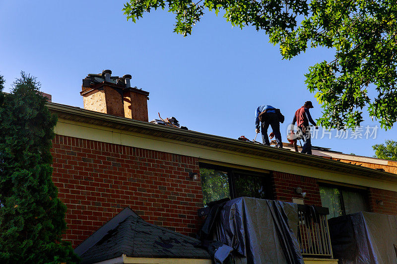 一名屋顶工人用气枪钉住瓦片，取代屋顶保护层