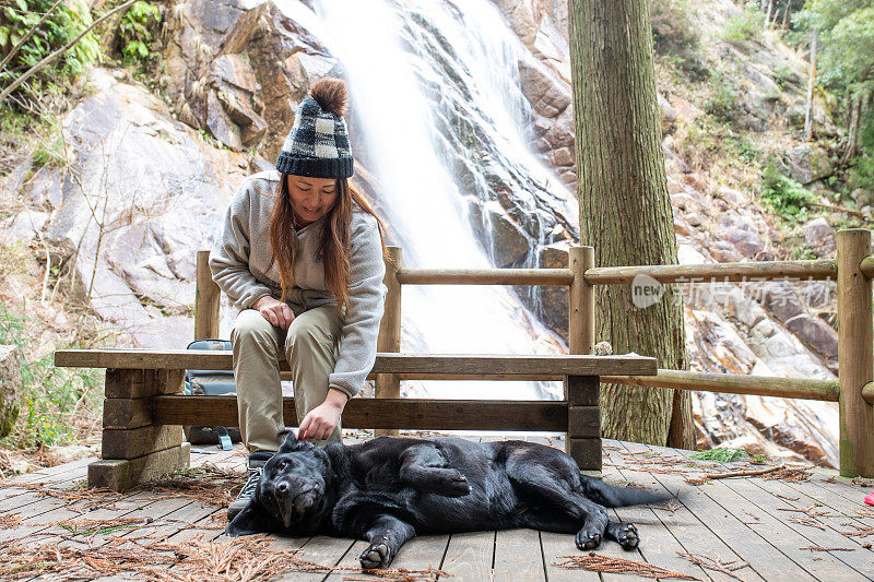 一个女人和一只狗坐在瀑布旁的长椅上