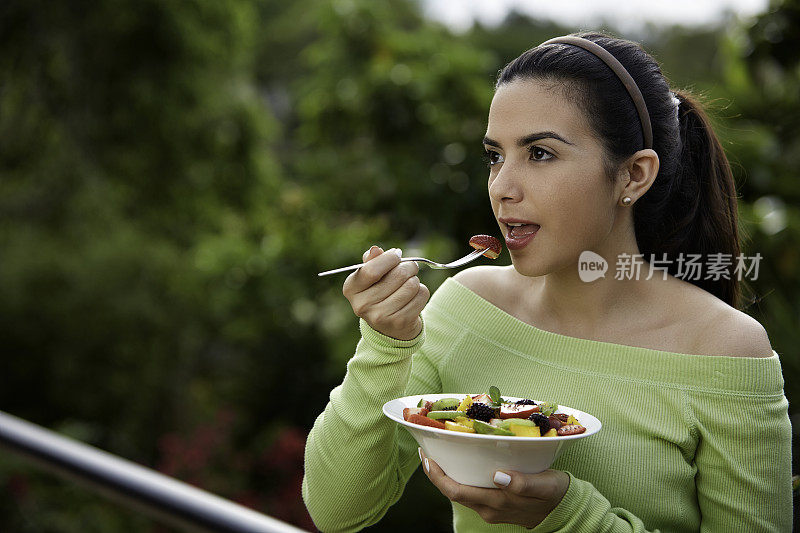 特写的一个西班牙可爱的年轻女人吃水果沙拉在户外午餐