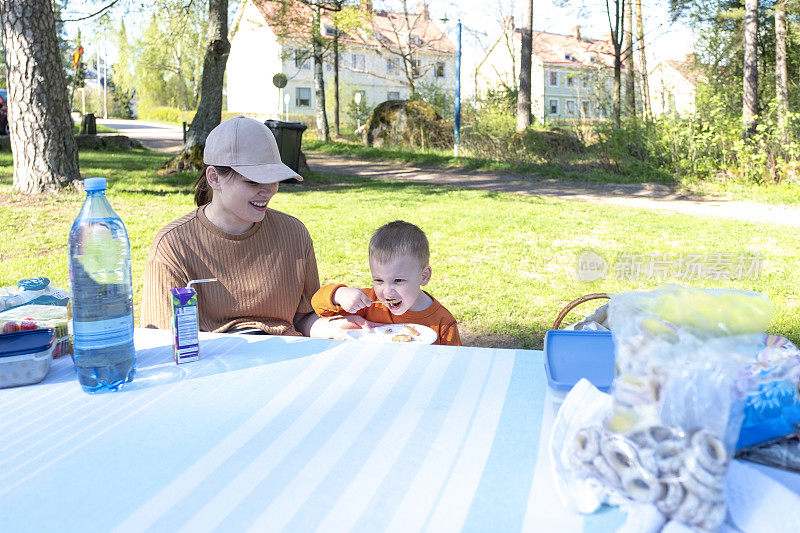带着孩子的女人在大自然中进食。在城市公园野餐。一个白人家庭，妈妈和3岁的儿子