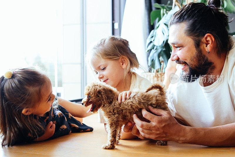 快乐的父亲和女儿们在沙发上玩他们的玩具卷毛狗