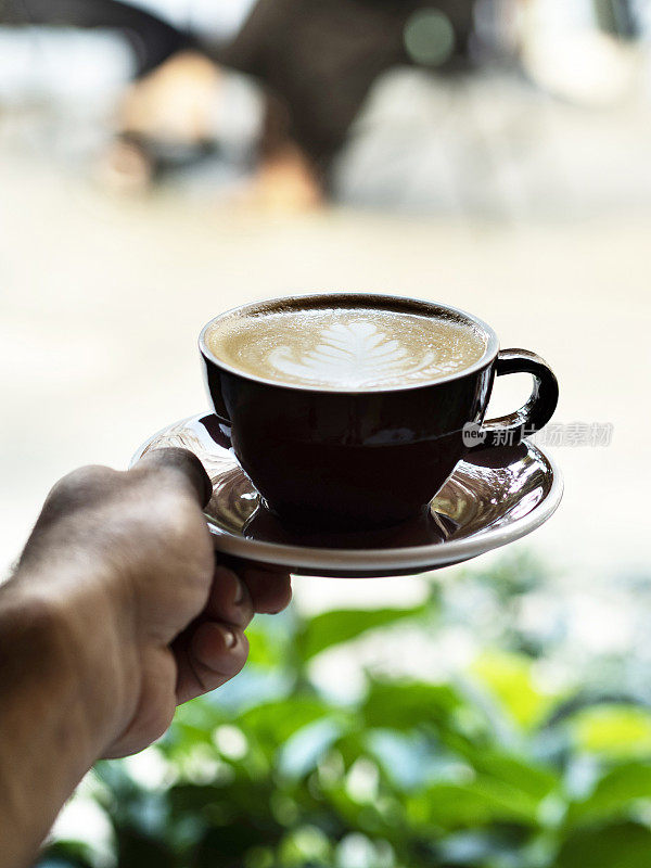 手捧一杯咖啡，男人的手捧咖啡杯在绿色的散景背景下，男人的手捧一杯棕色的热咖啡，男人的手捧一杯咖啡，