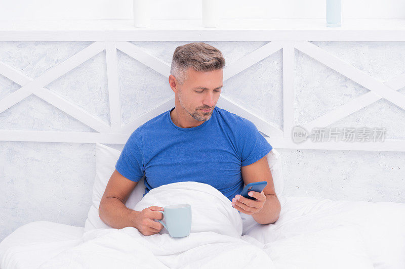 手机短信。醒着的男人在床上发短信。从智能手机的消息。发短信