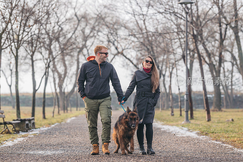 一对恩爱的夫妇和一只德国牧羊犬在散步