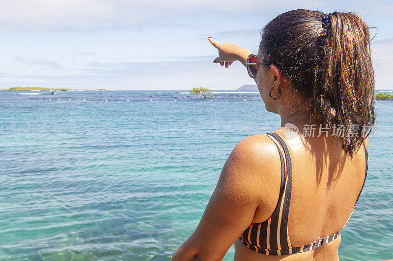 一个美丽的年轻自由放松的女人旅行，放松，发现和用她的手指指着孔查德佩拉礁海滩，伊莎贝拉岛，加拉帕戈斯岛，厄瓜多尔，拉丁美洲