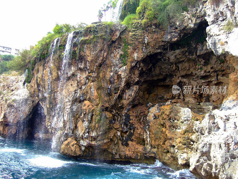 一条小瀑布沿石壁而下。悬崖顶上有绿色的灌木和树木