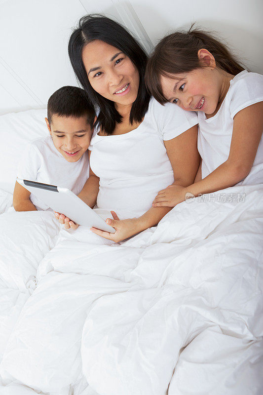 快乐的亚洲妈妈和孩子们在床上阅读