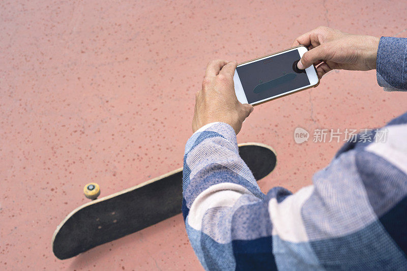 滑板园内，滑板少年用智能手机对着滑板拍照。