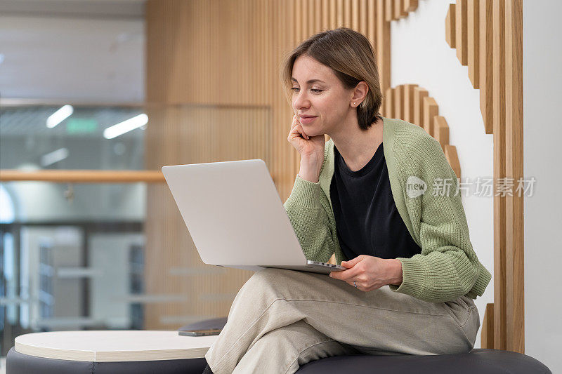 有思想的中年女性自由撰稿人使用笔记本电脑，在联合办公空间在线工作