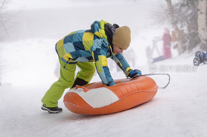 小男孩在雪管上从山上滑下来。