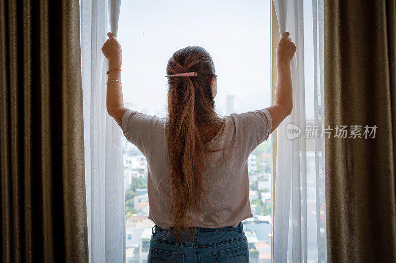从高楼的窗户往外看的年轻女子。