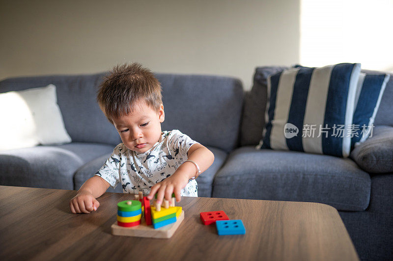 小男孩站在家里的桌子旁玩着五颜六色的分类和形状堆叠玩具