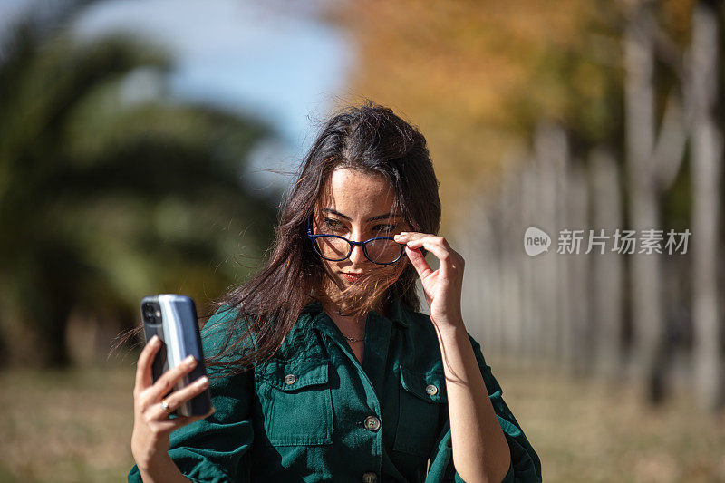 黑发女商人正在公园里工作。
她正在看她的手机。