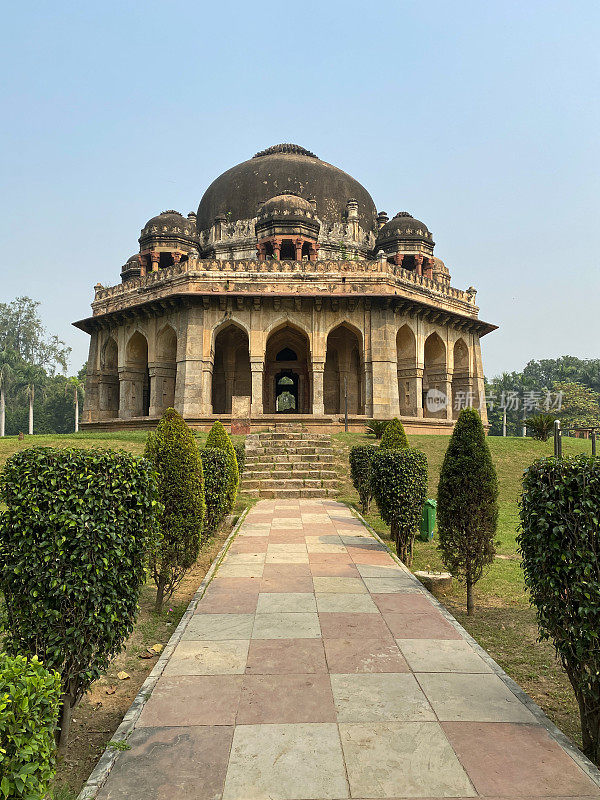 印度新德里，洛迪花园公园的特写图像，通往西坎达尔·洛迪历史陵墓墓的铺好的人行道，绿色的草坪，培育的花坛，修剪整齐的修剪树枝的云树