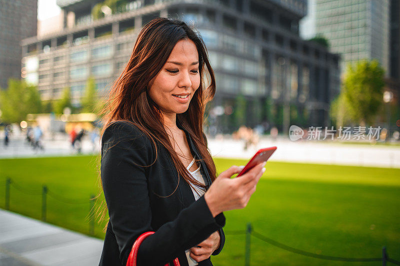 中年日本女商人在户外用智能手机发短信