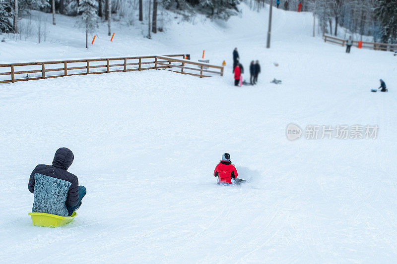 一个男人和一个女孩坐着雪橇从白雪覆盖的山上滚下来。周末户外娱乐。