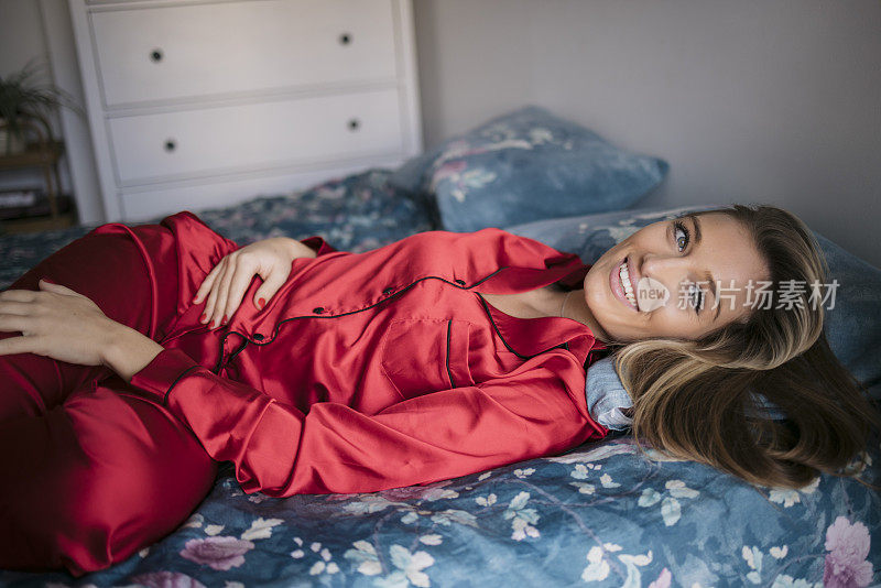 快乐的女性在红色睡衣躺在床上