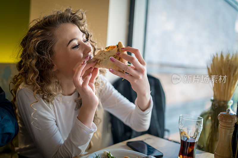 女人正从烧木头的炉子里吃披萨。在意大利餐厅吃午餐。