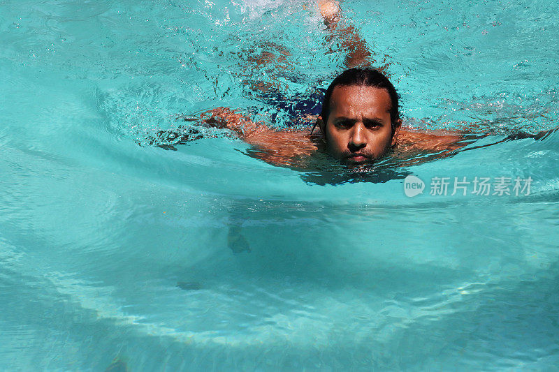 印度男子在清澈的水中做蛙泳的特写，室外，游泳池，绿松石蓝色马赛克瓷砖被波纹水扭曲，游泳和飞溅，波涛汹涌的水面反射，重点在前景
