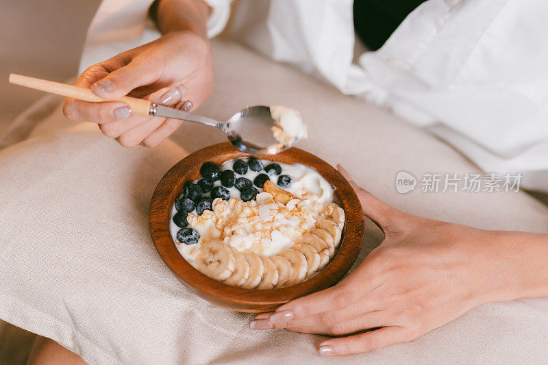 年轻的亚洲女性在家里客厅的沙发床上吃健康的早餐，有水果和酸奶