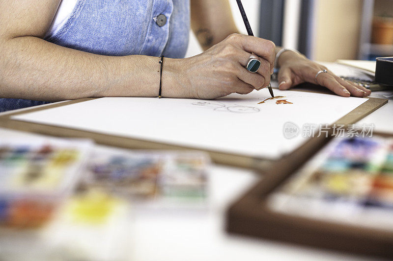 选择性地集中在一个插画家的手画她的作品在不同的水彩材料。