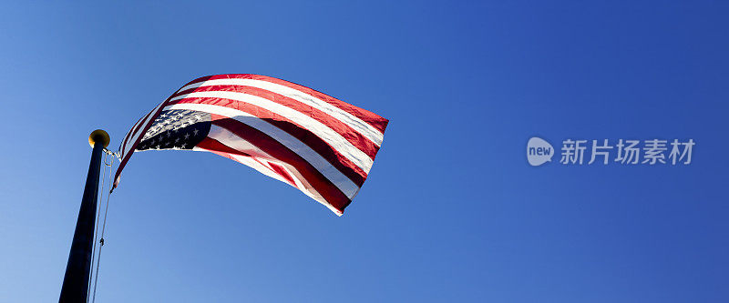 在晴朗的蓝天上，旗杆上飘扬着美国国旗