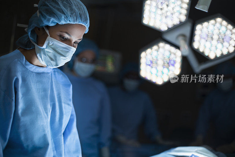 西班牙裔医学专业医生护士在医院的外科手术室与灯光和同事一起俯视病人