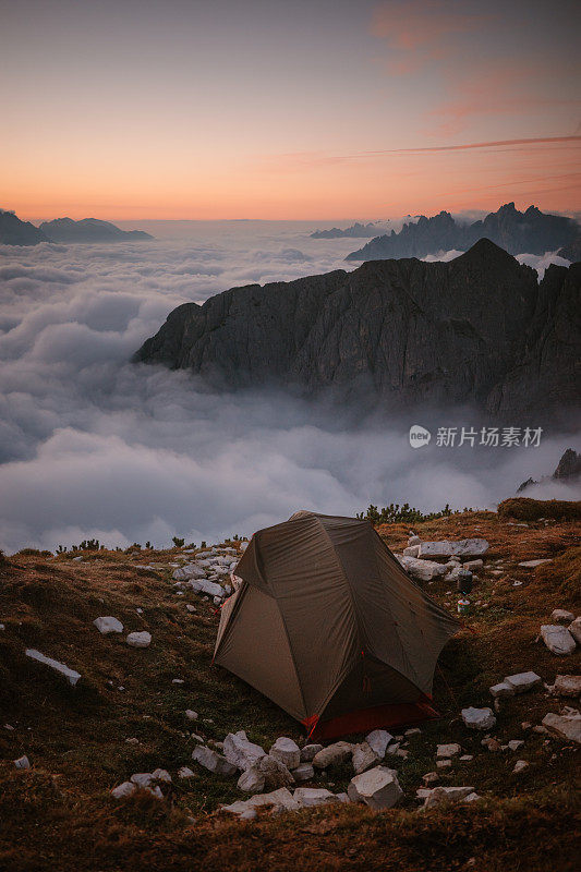 在白云之上的山顶上搭帐篷。在黄昏时徒步旅行到未知的地方