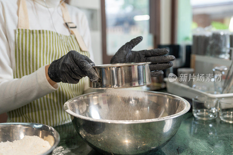 白种人或棕色头发的黑发白人妇女筛面粉准备烘烤。在她的咖啡馆工作场所开始新的生意或自己的生意。