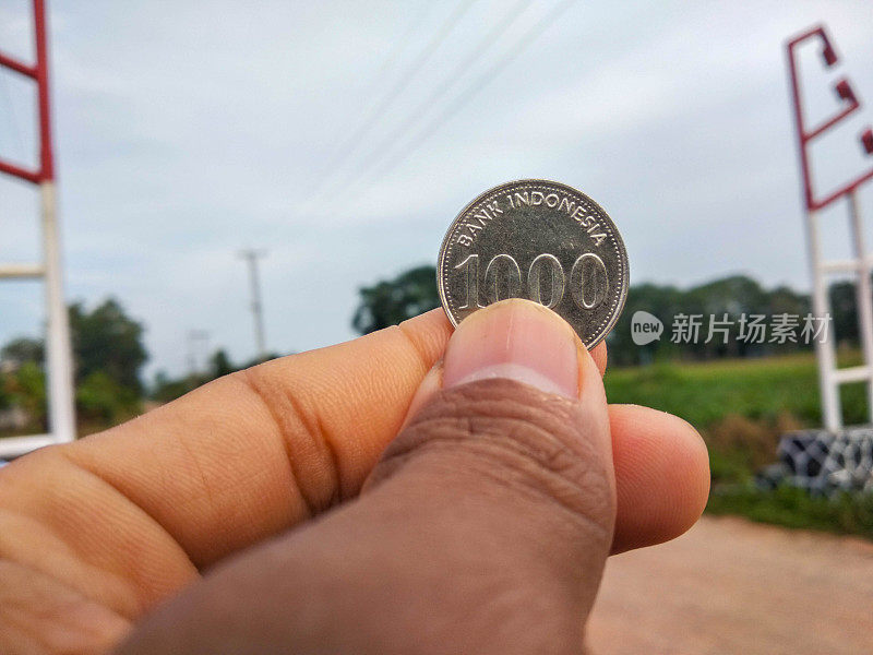 拿着一枚刻有1000印尼盾的硬币
