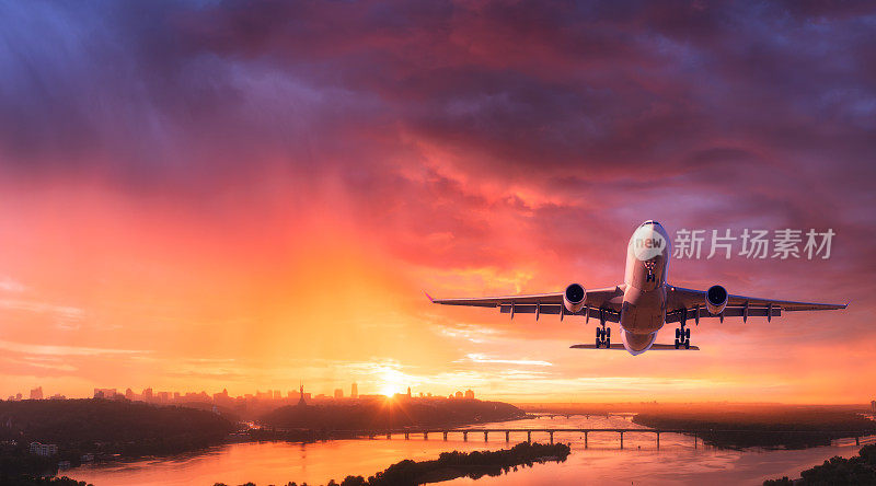 夕阳下，一架飞机在城市上空五颜六色的天空中飞行。有客机的风景，天际线，黄昏时紫色的天空和红色和粉红色的云。飞机将在黄昏降落。飞机鸟瞰图